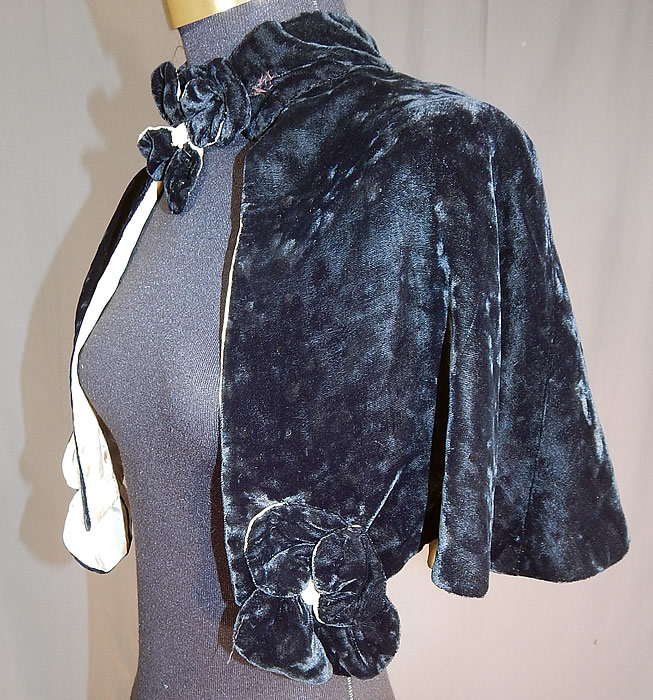 Vintage Black Silk Velvet Flower Trim Short Cropped Cape Evening Shawl Capelet
The cape measures 13 inches long, with a 14 inch neck and is 16 inches across the back shoulders. It is in fair as-is condition, with some small crush marks on the velvet fabric which has not been steamed, fraying along the edging of the top collar, with a small mended repair on the side of the collar, some small faint stains, tiny holes on the inside silk lining.