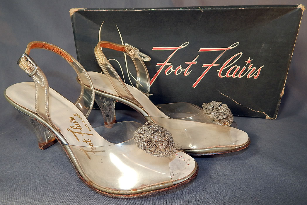Vintage Foot Flairs Beaded Clear Carved Lucite High Heels Slingback Shoes
They are made of a clear plastic vinyl instep, with silver crystal beaded rosette trim on the vamps and carved clear lucite high heels. 