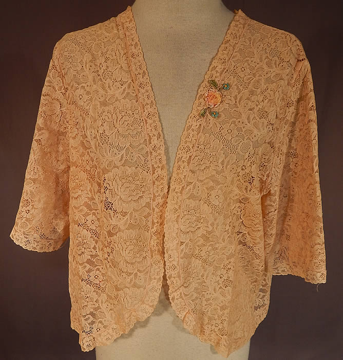 Vintage Silk Pastel Rosette Trim Cream Lace Bolero Boudoir Bed Jacket
This vintage silk pastel rosette trim cream lace bolero boudoir bed jacket dates from the 1930s. It is made of an off white cream color sheer lace fabric, with a floral leaf pattern and a small silk pastel ombre rosette ribbon work appliqué trim sewn onto the lapel. 