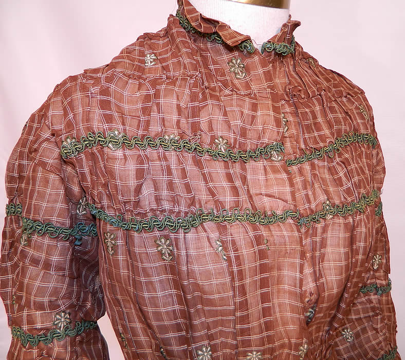 Victorian Civil War Brown & White Plaid Muslin  Green Floral Trim Embroidered Dress. It is made of a brown and white stripe checked plaid sheer muslin fabric, with a green floral embroidered daisy design and green braided trim edging. 