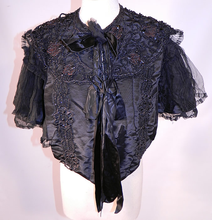 Victorian Black Silk Jet Beaded Mourning Mantle Dolman Cloak Cape Capelet
This antique Victorian era black silk jet beaded mourning mantle dolman cloak cape capelet dates from 1880. It is made of a black silk fabric, with jet beaded trim appliques and a pleated black sheer silk chiffon fabric sides.