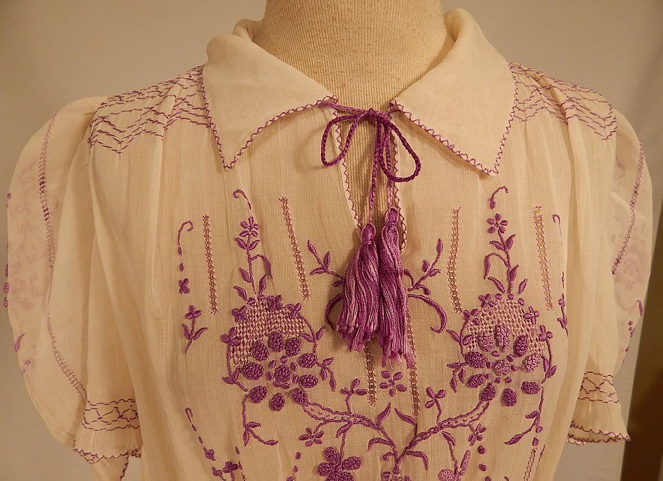 Vintage White Cotton Purple Embroidered Smocking Boho Peasant Drop Waist Dress
This pretty peasant style bohemian Hungarian Czech dress has a drop waist style, with smocking detail around the waist, shoulders with gathering, short puffy sleeves, a fold over collar, with tassel tie front neckline, side snap closures and is sheer, unlined. 