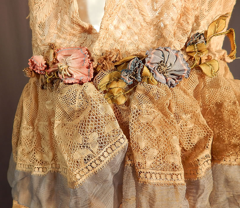 Vintage Cream Tambour Embroidery Lace Silk Rosette Drop Waist Dress
There are colorful pastel silk ombre wired rosette ribbon work flower trim accents around the neckline, hanging down the back tie sash and along the side hip area. This fabulous flapper dress has a loose fitting straight shift chemise style, with a drop waist, an attached blue chiffon necktie scarf with rosette trim ends hanging down the back, sleeveless, with an open side top, no closure, sheer, unlined and a layered tiered ruffle long tea length skirt. 