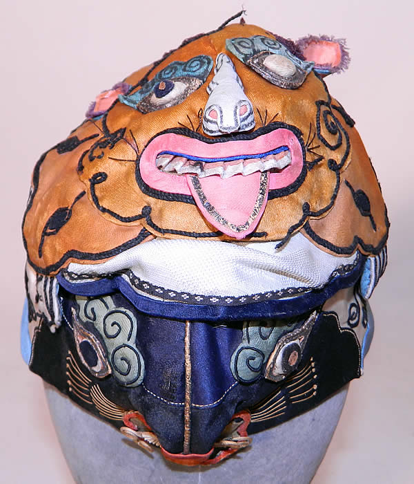 Antique Chinese Child Infant Silk Applique Tiger Wind Hat. It is hand stitched, made of colorful silk fabrics, with an appliquéd tigers face on the front and on the top, with peaches and flowers appliquéd on the sides and back. This unusual animal shaped hand crafted hat has two different detailed 3 dimensional faces of a smiling grinning tiger, with it's ferocious powers make it an especially popular protective image and would have been used to frighten off evil spirits. 