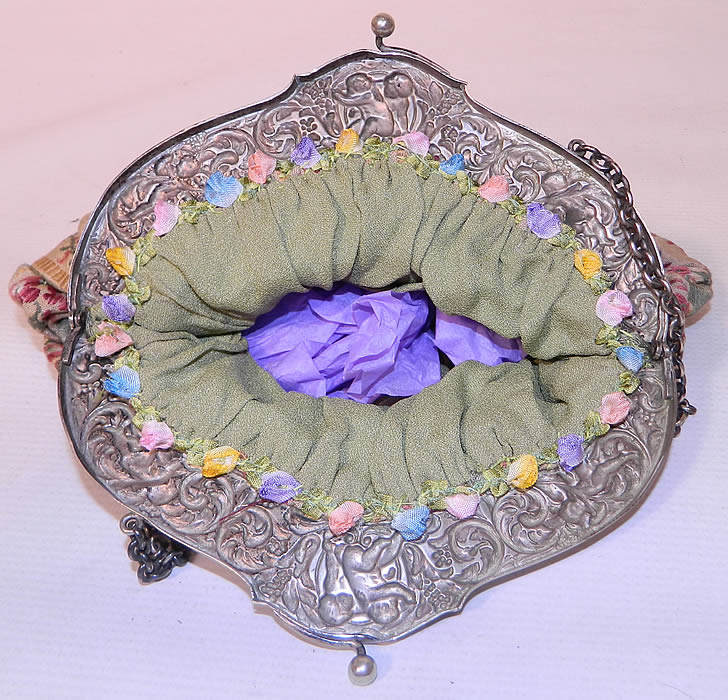 Antique Silver Plate Repousse Cherub Cupid Frame French Silk Brocade Fabric Purse. The purse is made of a colorful striped silk damask brocade fabric with a floral pattern design and is fully lined in green silk with pastel silk rosette floral trim edging sewn inside. 